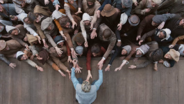 Film still from Hamnet (2025). Image of a crowd reaching up to an actor on a stage during a performance of the play, Hamlet.