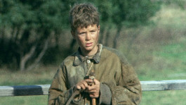 Film still from Pelle the Conqueror (1987). Image of a young boy standing against a fence.